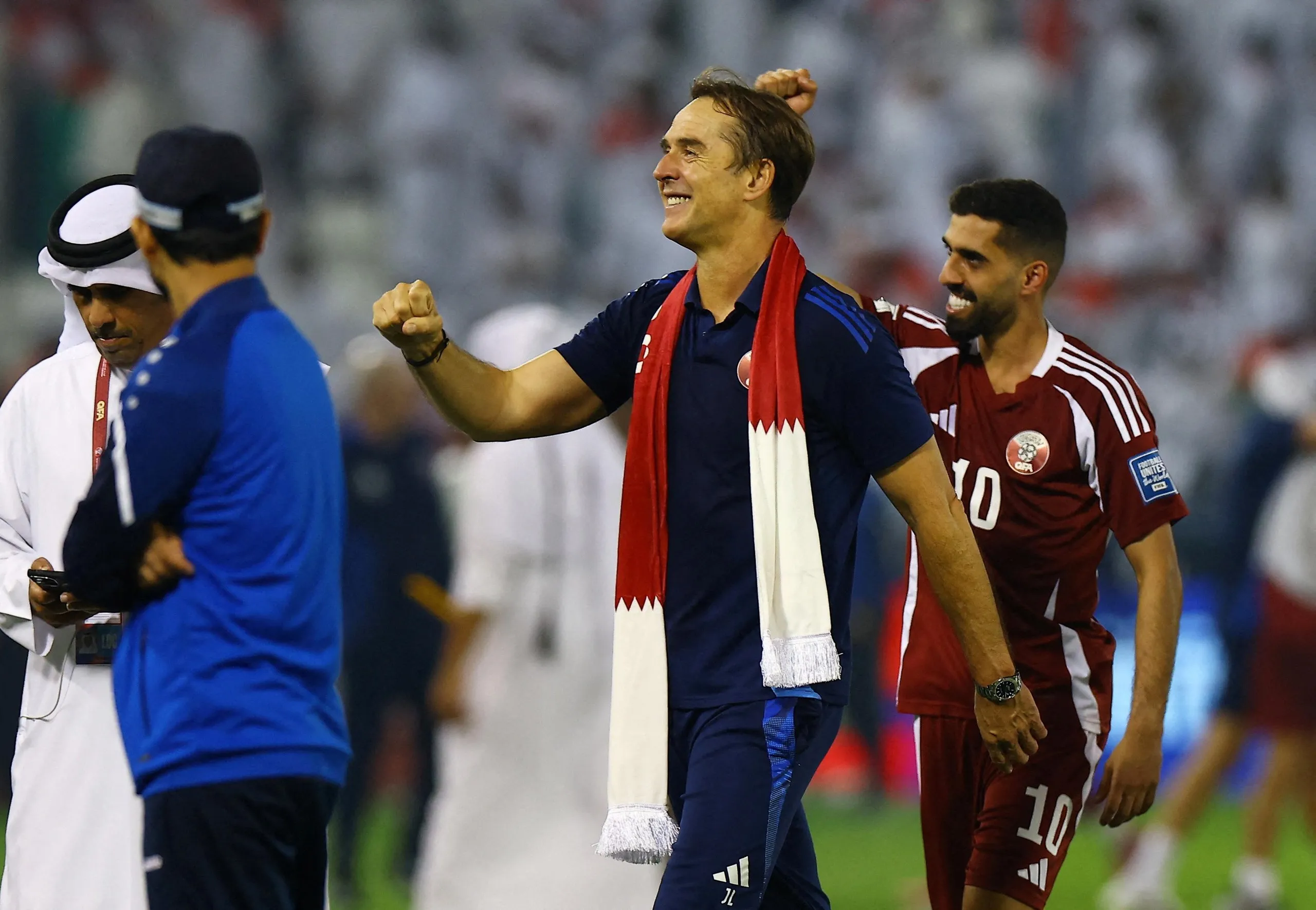 Julen Lopetegui, the Qatar men’s football head coach, pumps his fist in celebration of his team qualifying for the 2026 World Cup. He has a scarf in the colours of the Qatari flag around his neck.