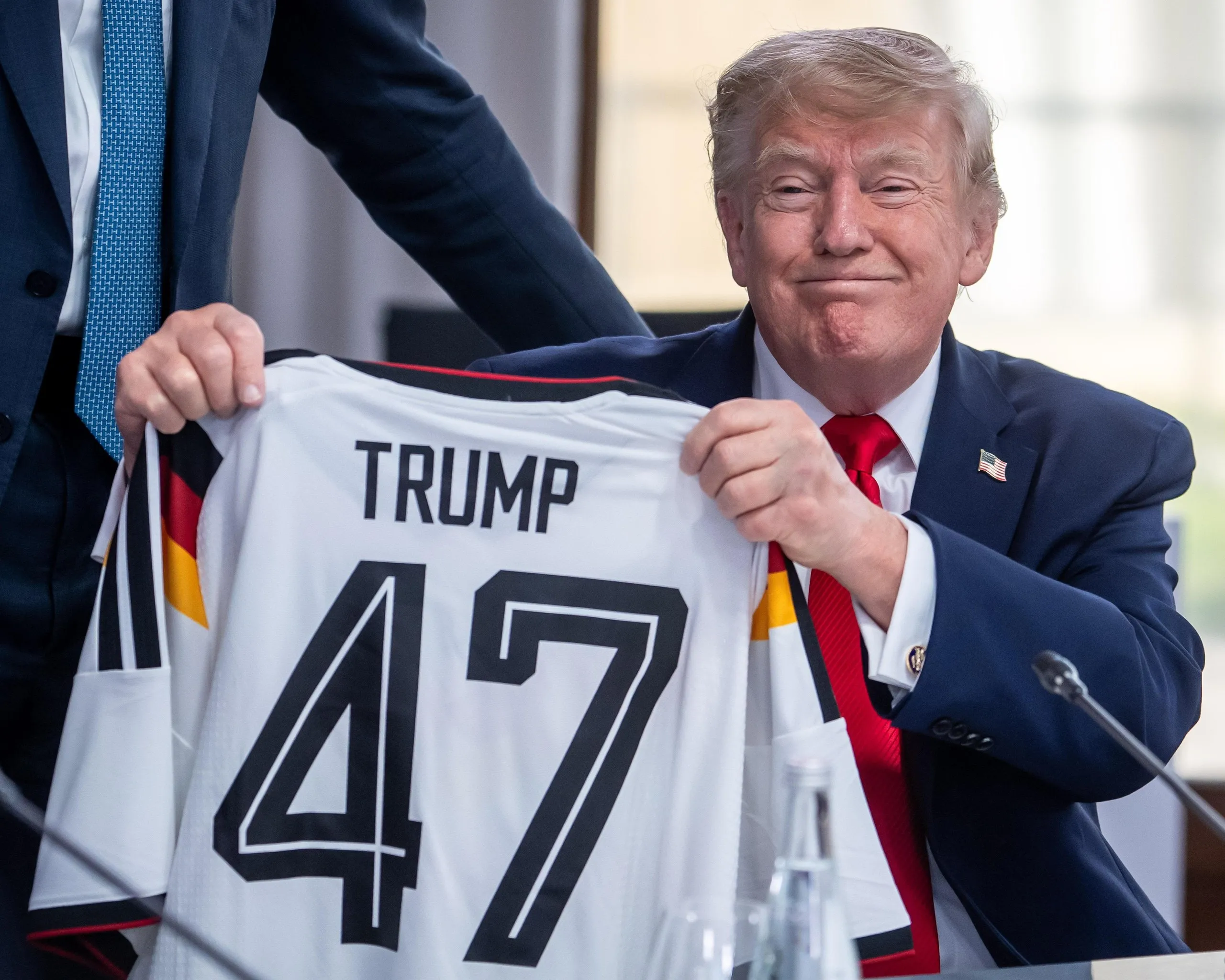Donald Trump holds up a Germany top that he received as a gift from Friedrich Merz