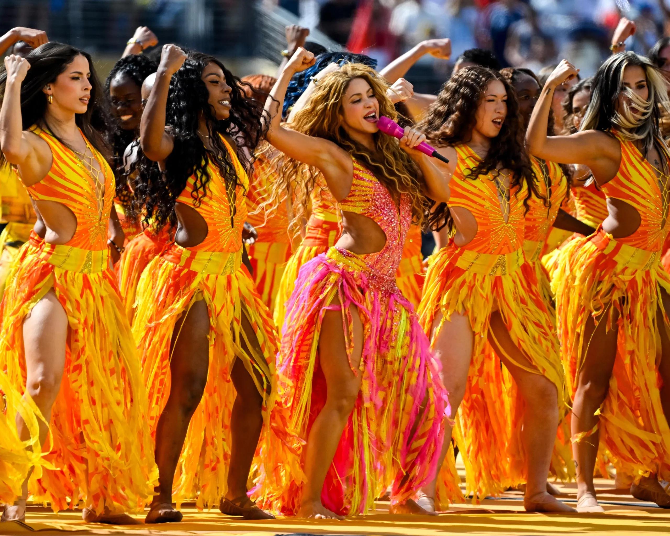 Shakira and a row of dancers in orange outfits